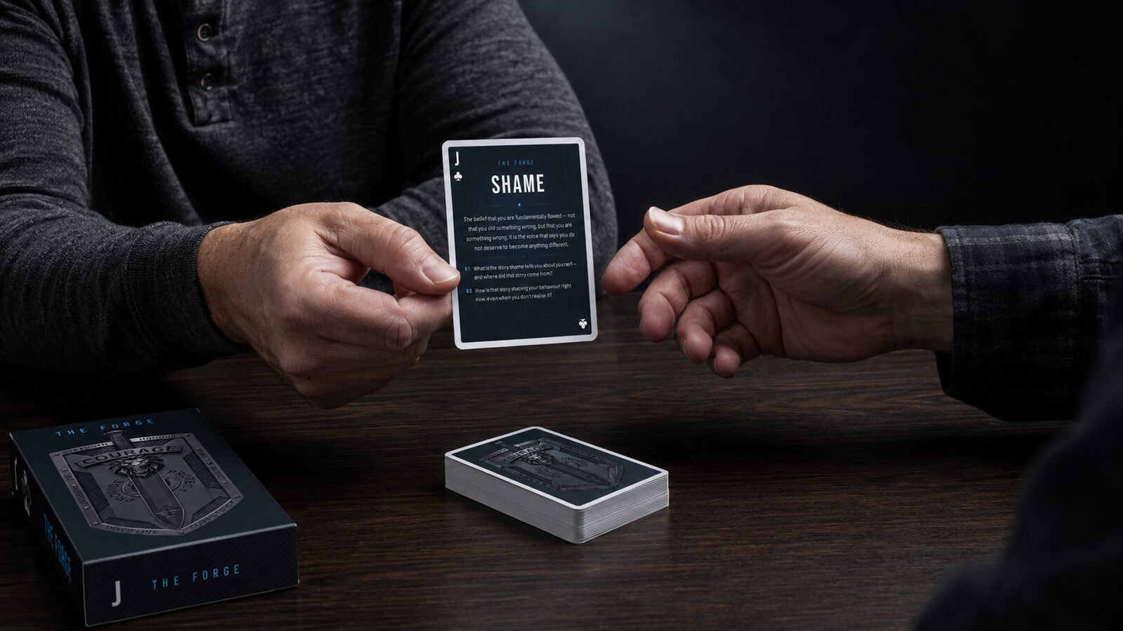 One man holding the Shame card out to another across the table.